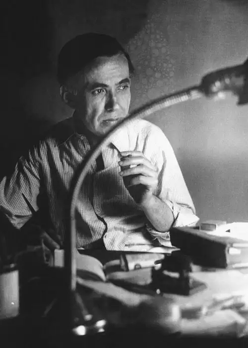 Behçet Necatigil, çalışma masasında derin düşüncelere dalmış halde, elinde kalemle şiir yazarken.