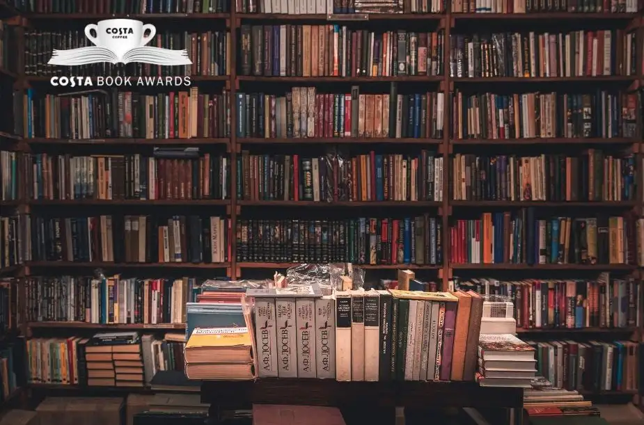 Costa Book Awards logosu eşliğinde kitaplarla dolu bir kütüphane rafı – edebiyat ödüllerini temsil eden nostaljik bir atmosfer.